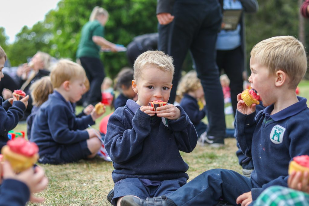 Students and staff of Langley School enjoying a VE Day picnic with a variety of food and smiling faces.